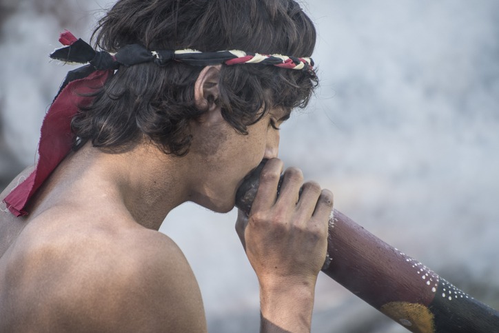 young man plays the didgeridoo at Mardi Grass parade.