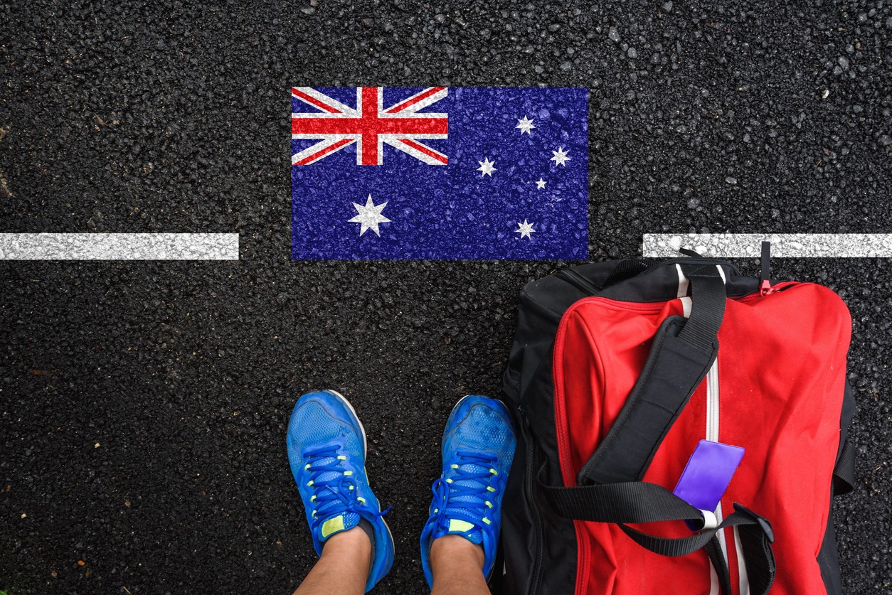 a man with a shoes and travel bag is standing on asphalt next to flag of Australia and border