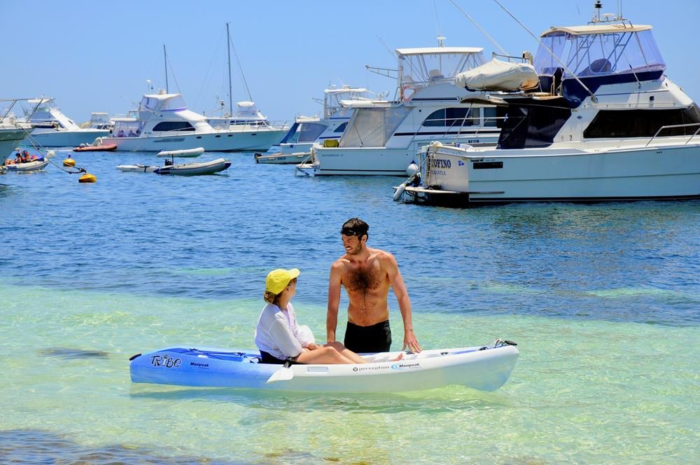 A young couple enjoying the beach at Rottenest Island in Perth, along with yachts moored off the beach