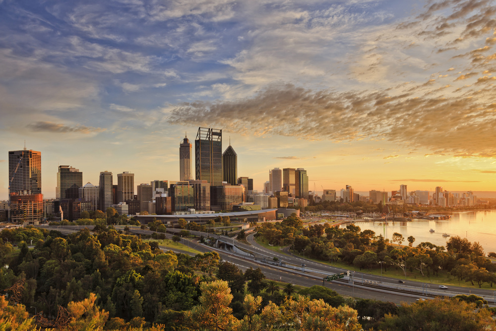 Gold warm sun light litting CBD of Perth city as seen from Kings park with green trees and highway entering the city